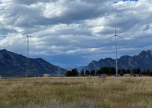 Multiple turbines in a field outlined by mountains. 