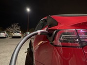 Red electric vehicle connected to a North American Charging Standard (NACS) -- now standardized as SAE J3400 -- direct-current fast charging cable.