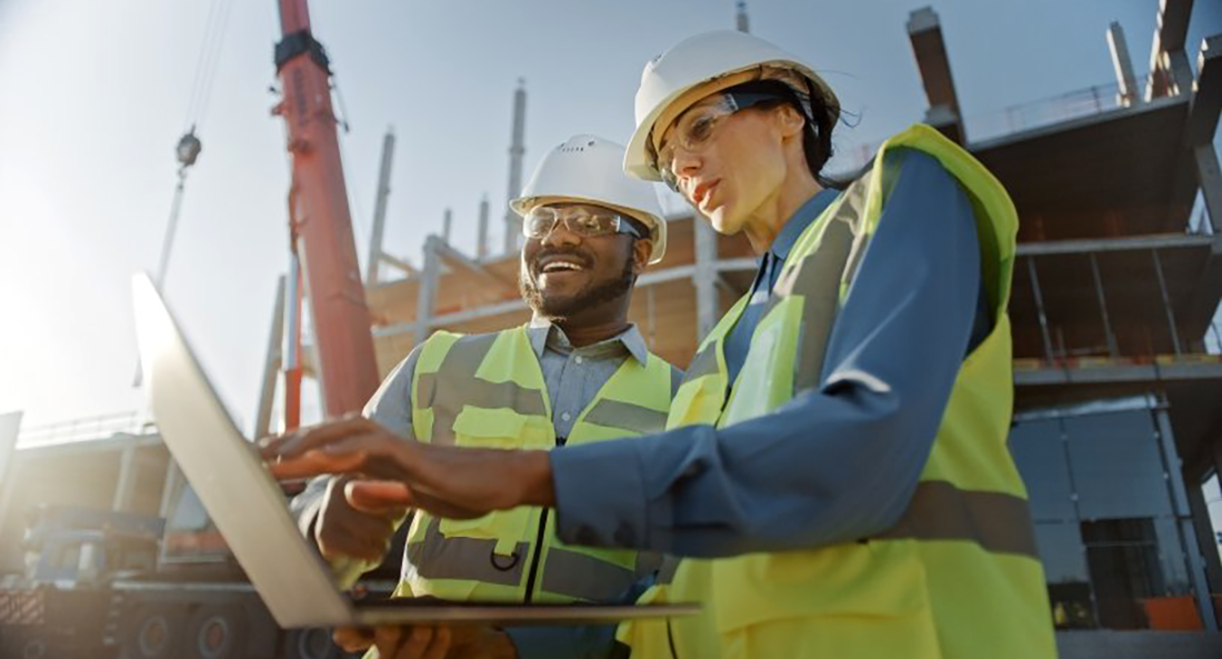 Two clean energy professionals in hard hats reviewing plans.