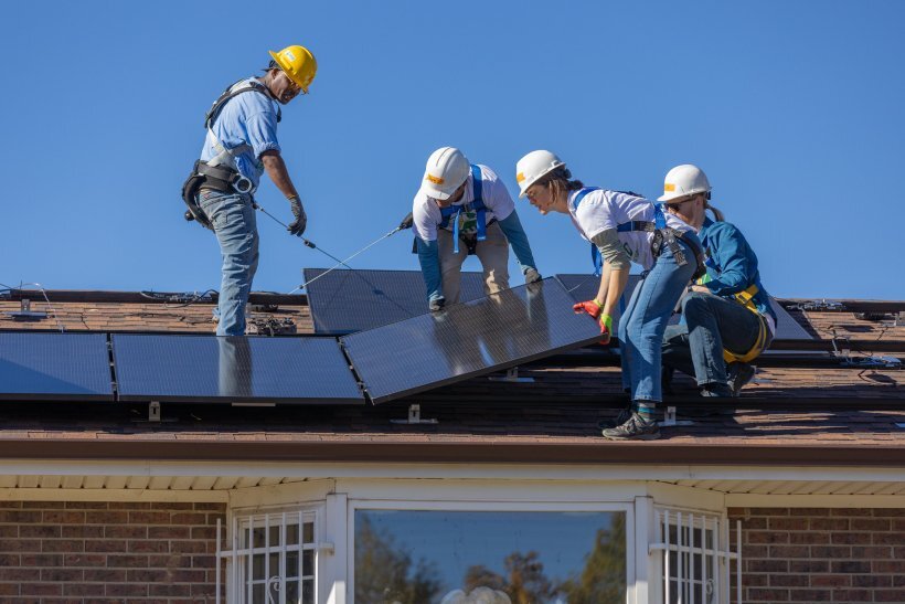 Solar installers lay photovoltaic panels on a residential roof.