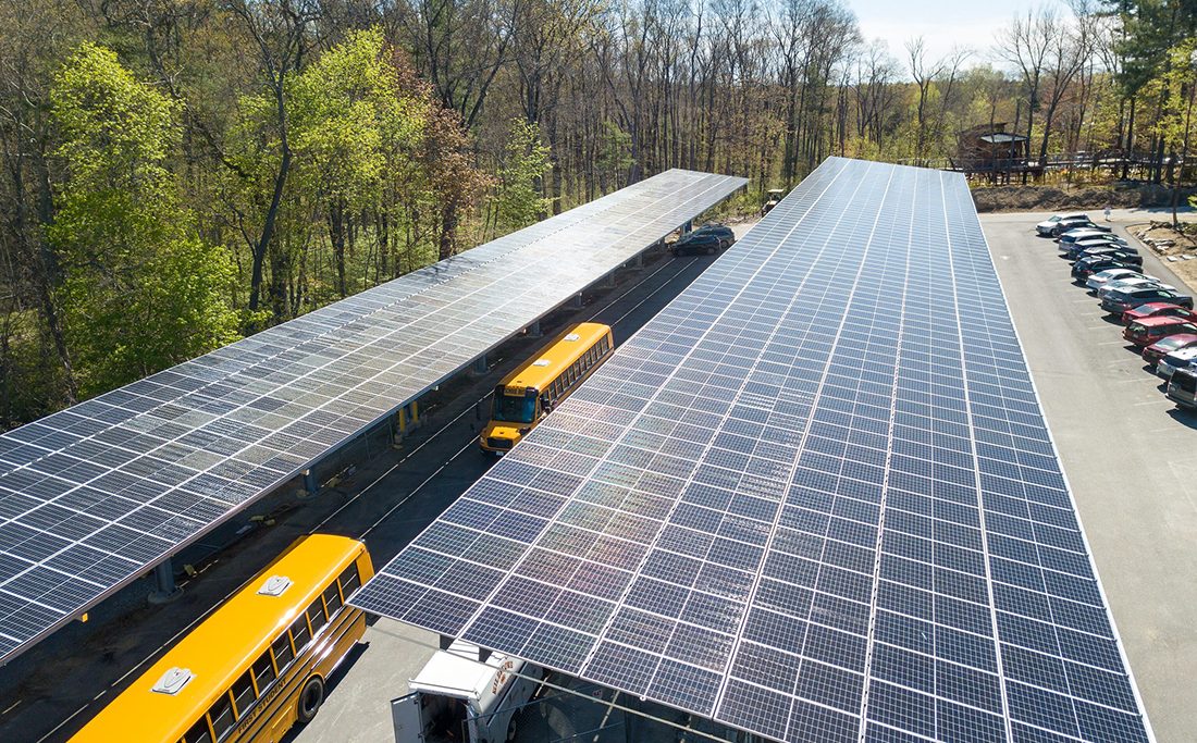 Two school buses drive below community solar arrays at the Discovery Museum in Acton, MA. Photo credit: Rachel Gentile