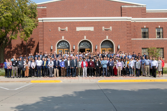 Large group of people pose in front of building. 