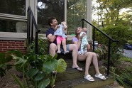 Mother and father hold their child in front of their house. 