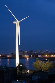 A turbine in front of a river on the other side of which is a city at night