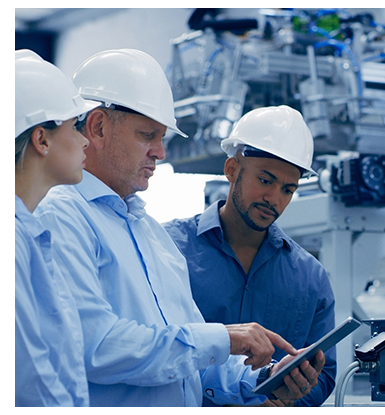 Three colleagues in hard hats review tablet in manufacturing plant