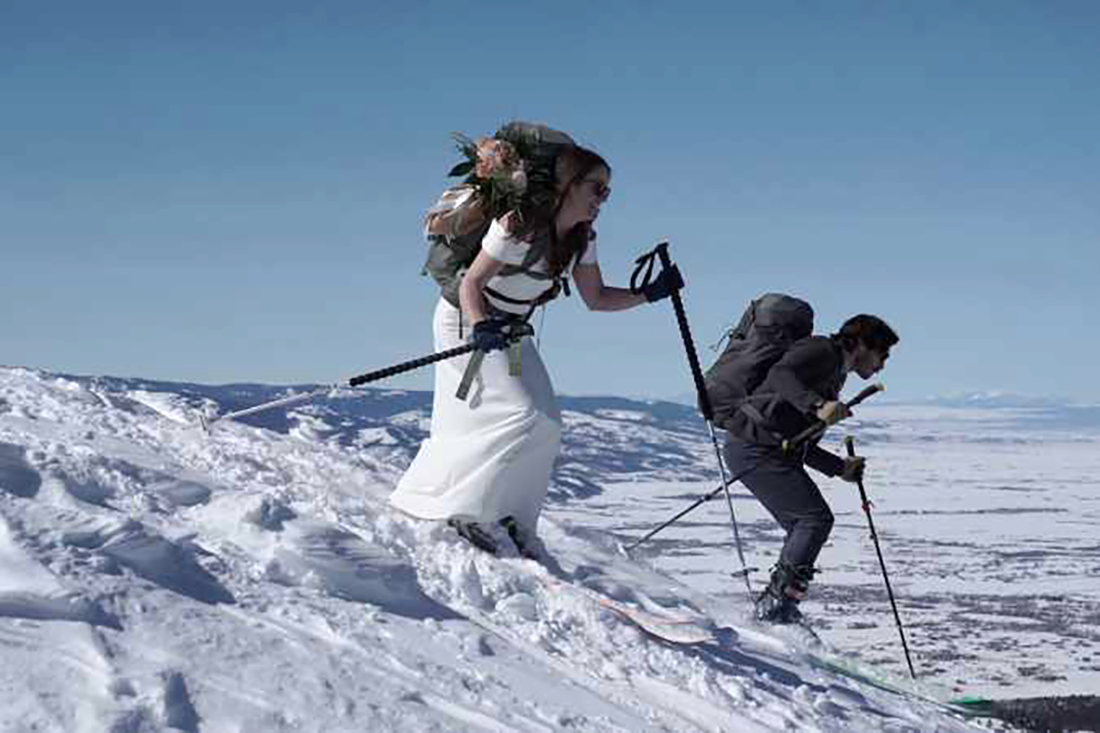 Juan and his wife ski down a snowy mountain in wedding attire.