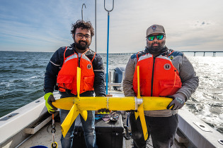 Two people holding a marine technology device while on a boat in the open water