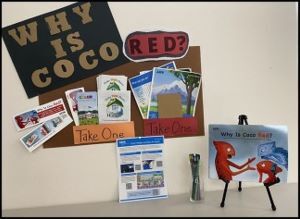 “Why Is Coco Red?” display board with flyers, photos, and “Take One” materials on stands.