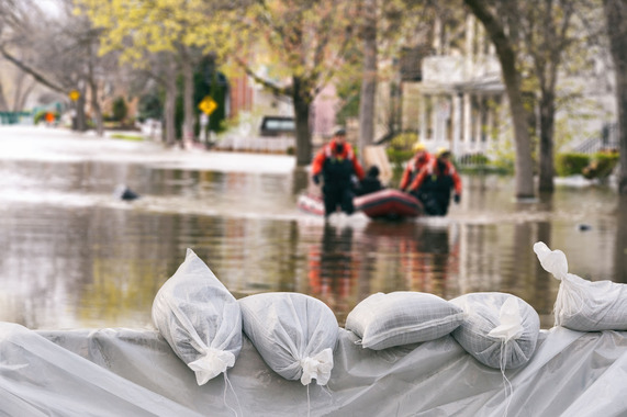 Four people with inflatable raft wading through knee-high water in suburban neighborhood