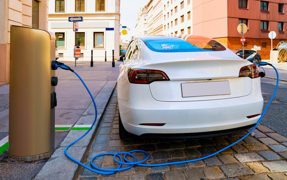 White electric-powered car parked on a city, plugged into a charging station.