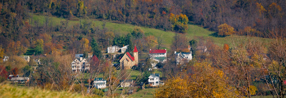 Far photograph of small rural town with wooded background. 