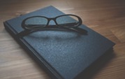 Black Framed Eyeglasses and book resting on top of wooden table