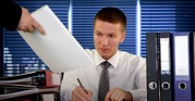 businessman seated at desk being handed paperwork