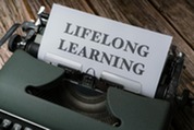 typewriter on top of wooden table with a piece of paper saying "LIFELONG LEARNING" in all capital letters