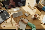 Person Writing on Notebook in front of a computer in a virtual meeting