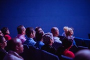 Group of people sitting in chairs in a dark auditorium 