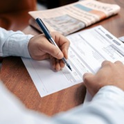 A person holding a pen filling in documents on a wooden desk