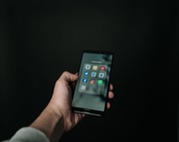 Person holding a smart phone in their left hand looking at social media apps in front of dark background