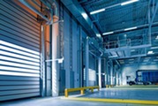 A brightly lit warehouse interior with multiple loading docks, yellow safety barriers, and a white truck backed into one of the bays.
