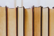 Row of old hardcover books standing upright, showing worn yellowed pages and dark spines close together.