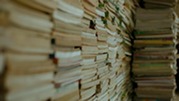Stacks of books piled closely together, creating a narrow aisle that suggests a large volume of reading or training materials.