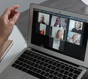 Person participating in a virtual meeting on a laptop with multiple attendees visible on screen.