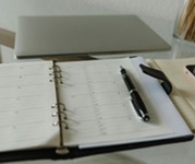 Open planner with pen on a desk beside a laptop and notebook, suggesting scheduling, planning, and professional work.