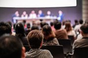 Audience members watch a panel discussion in a conference room.