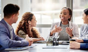 Four professionals sit around a conference table discussing ideas, with one person gesturing while the others listen.