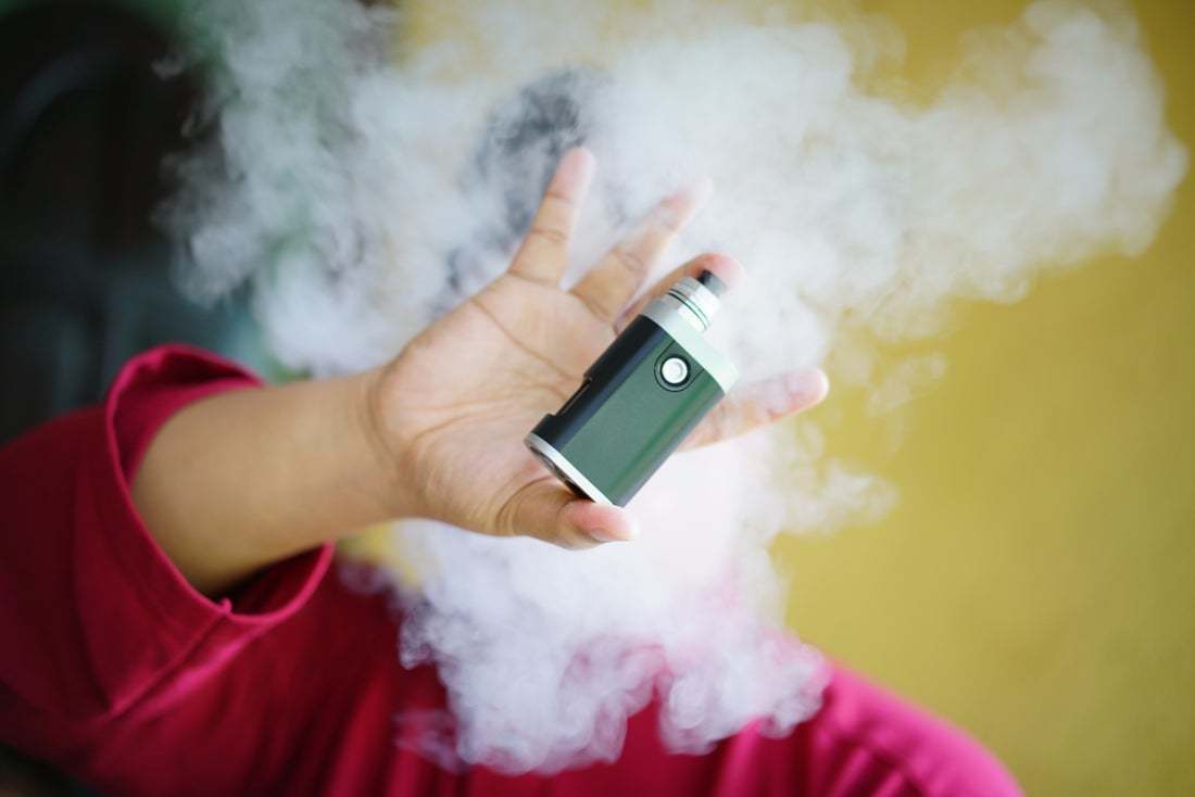 image of a person in a cloud of smoke holding an e-cigarette cartridge 