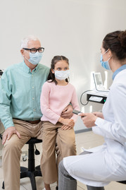 Man and his granddaughter wearing masks and talking with a doctor