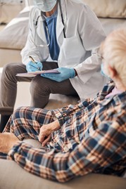 An older man sitting on a chair and talking with a health care provider.