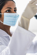 A woman wearing a lab coat, face mask, and gloves analyzing a sample.