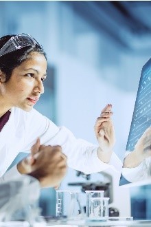 Photo of man and a woman wearing lab coats and looking into a computer screen. 