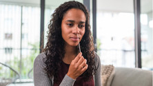 A woman performing a nose swab as part of a COVID at home test.