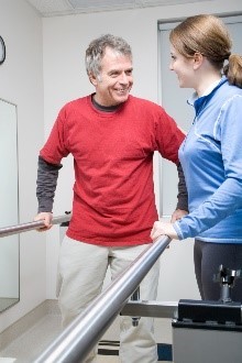 A woman helping a man walk on crutches in a hospital. 