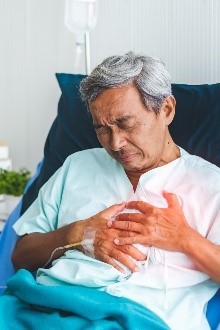 An older man holding his heart with both hands, as he is with chest pain. 