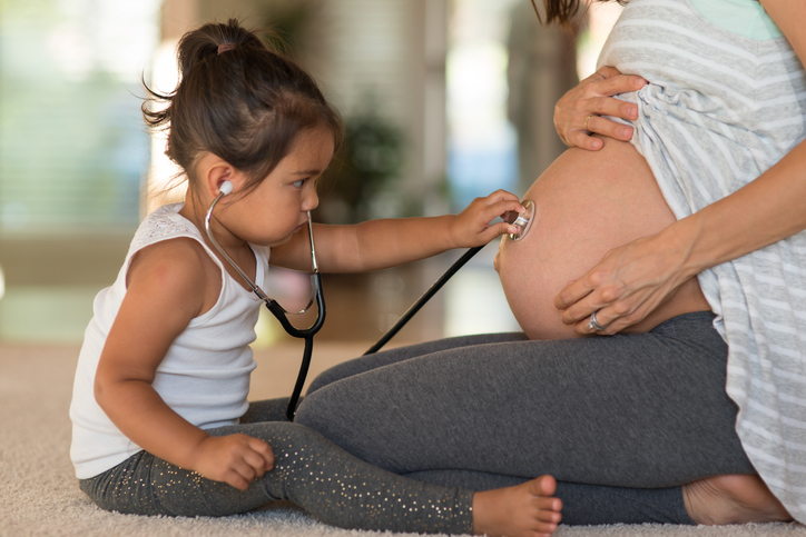 Toddler listening to pregnant mother's belly with a stethoscope