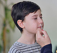 Child getting nose swab for COVID-19 at-home OTC test, assisted by adult