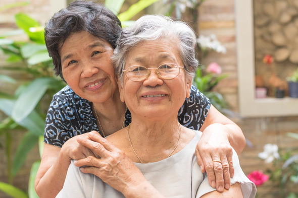 Two older woman - mother and daughter smile as they embrace one another.