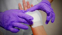 A person with gloved hands applying a bandage onto a person's wrist.