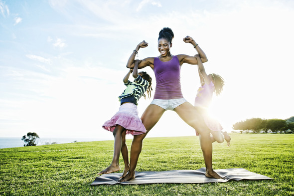 An African American mother dressed in exercise clothing plays with her two daughters outside