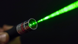 A green laser beam shoots from a hand-held laser pointer. 