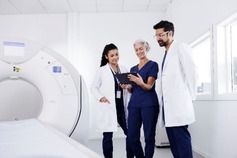 Three healthcare professionals standing next to a CT machine.