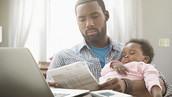 a father looking over bills, while holding his infant child