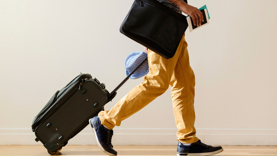 Photo: Sideview of a person wearing yellow pants walking with their suitcase.