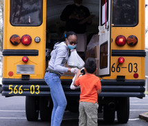 Young boy receiving school meals delivered by school staff from a school bus