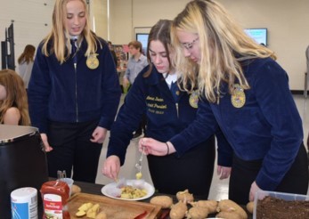 Three girls in FFA jackets doing a local food taste test
