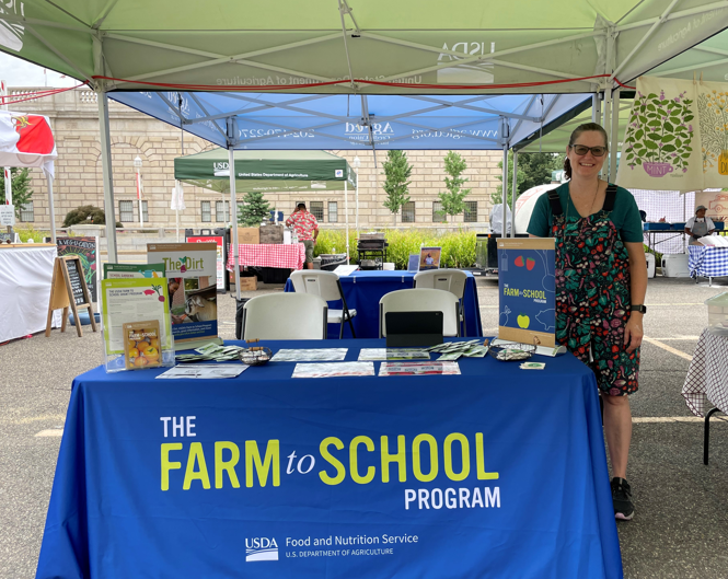Farm to School Program director, Julie Brewer standing at the Farmer's Market at the Farm to School Program Table