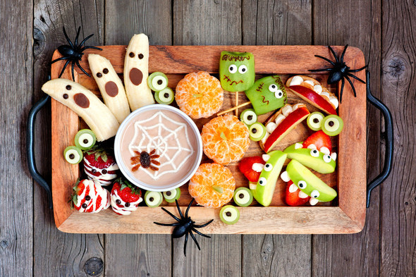 Tray of bananas, apples, oranges, and strawberries decorated with a halloween theme.
